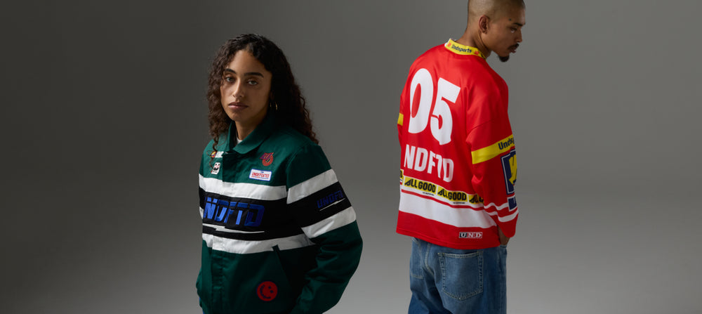 Two models wearing UNDFTD brand jerseys, one in a dark green colorway and the other in a red colorway, shown from the front and back against a dark gray studio background.