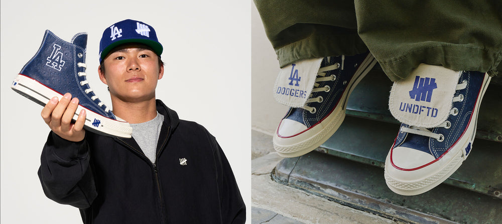 Person holding a blue and white sneaker with 'UNDEFEATED' branding, wearing a matching cap.