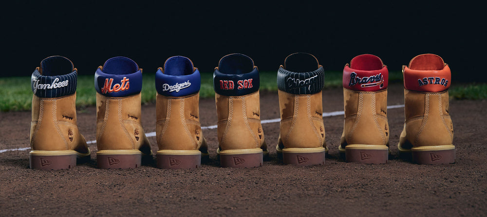 Six tan leather boots lined up on a baseball field dirt, each with a different sports team collar: Terry Fox, Mets, Dodgers, Red Sox, Navy, Arizona, and Astros.