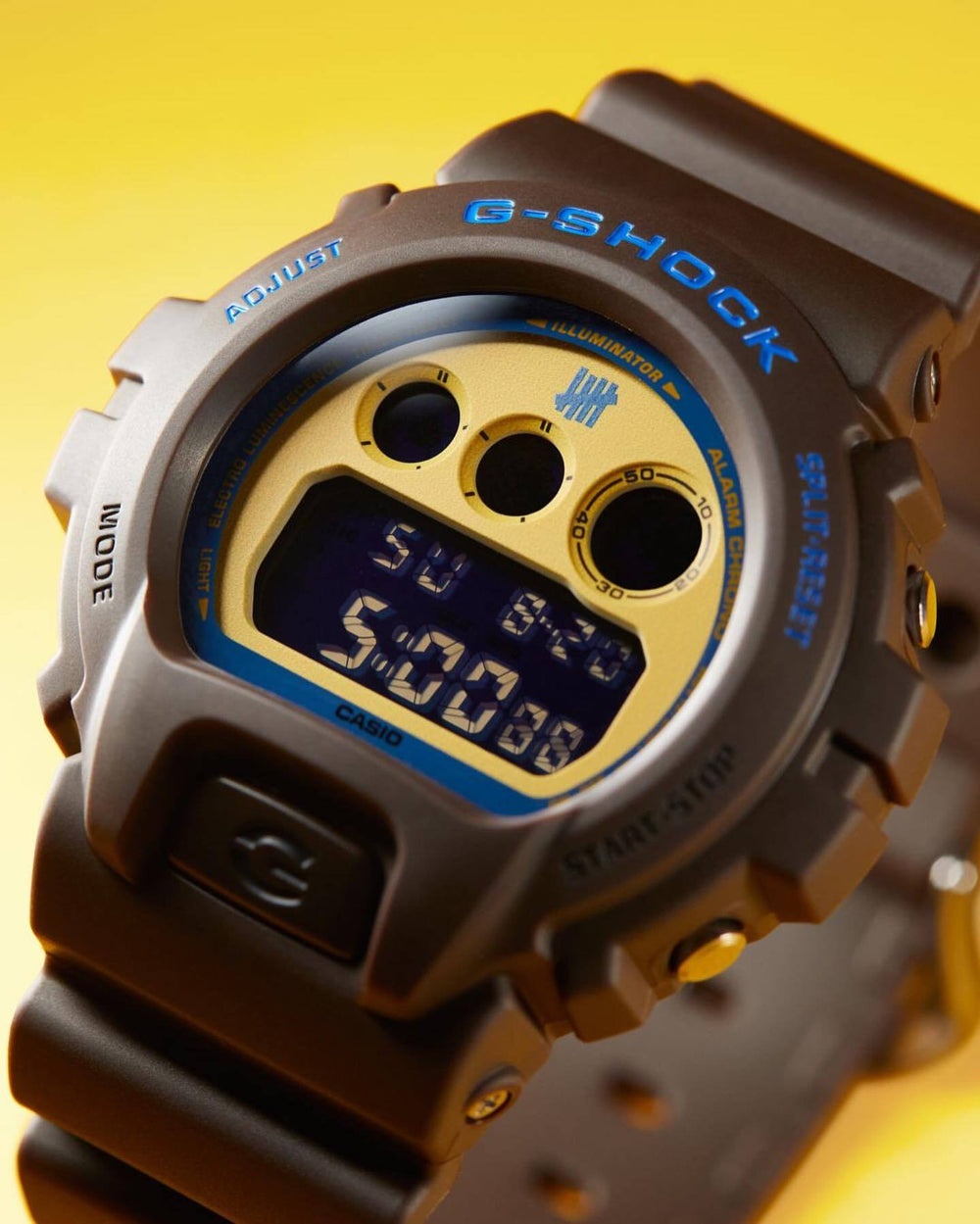 G-Shock digital watch with brown and gold accents on a yellow background